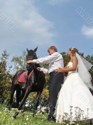 Happy newlyweds with horse outdoors