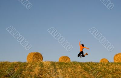 Woman jumping in a hay bales field