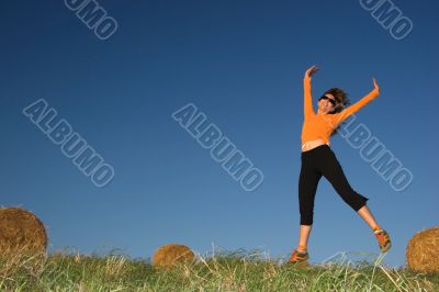 Woman jumping in a hay bales field