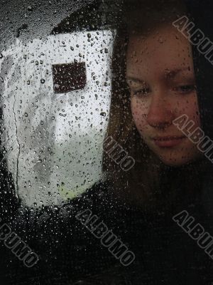 Girl looks thru waterdropped widow glass