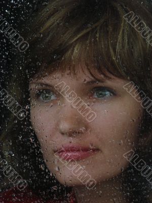 Girl looks thru waterdropped widow glass