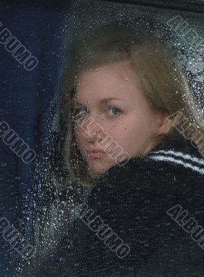 Girl looks thru waterdropped widow glass