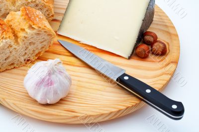 Cheese, bread, hazelnuts and knife on wood plate