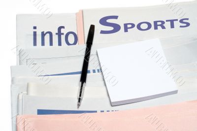 Note and pen, over stacked sports newspapers