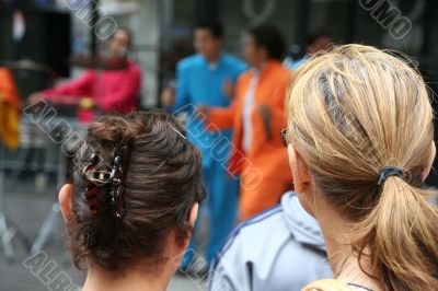 Two young women watching samba band