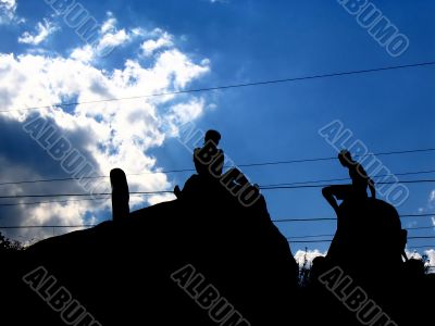 shapes of two people seated on a rock in the sky