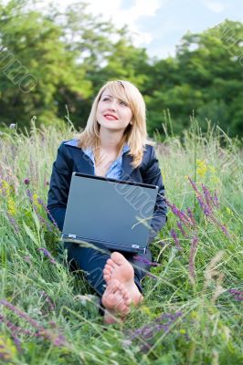 Businesswoman on grass with laptop and take off shoes