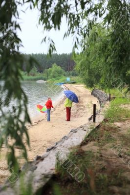 Mother and daughter with umbrella walking on riverside under rai