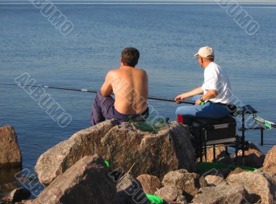 Seated men fishing off a shoreline