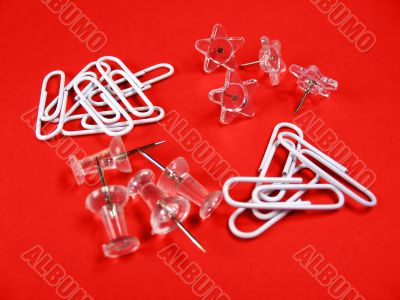 Paper clips and push pins over red background