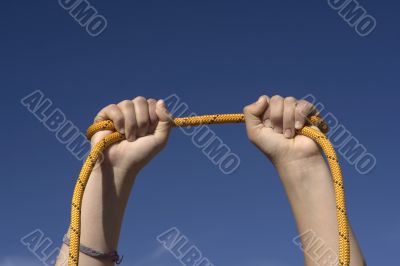 Two hands with an orange rope on sky background