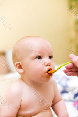 Mother feed baby by mashed melon and carrot with plastic spoon