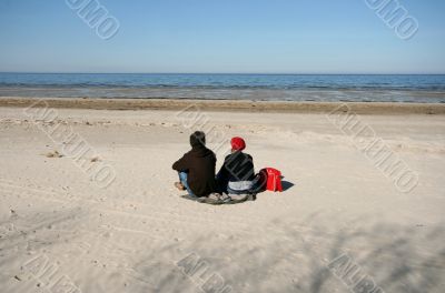 Woman and Man Sitting on Sand Watching Sea in Spring