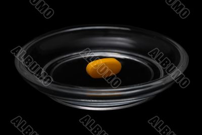 Yellow pill in bright glass saucer isolated on black