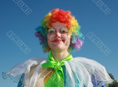 Expressive clown in colored wig upon blue sky