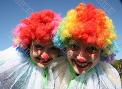 Two bizzare clowns in colored wigs upon blue sky