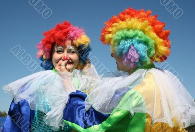 Two bizzare clowns in colored wigs upon blue sky