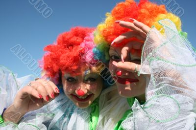 Two bizzare clowns in colored wigs upon blue sky