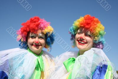 Two bizzare clowns in colored wigs upon blue sky