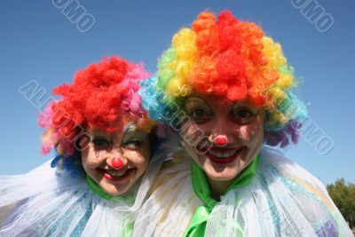 Two bizzare clowns in colored wigs upon blue sky