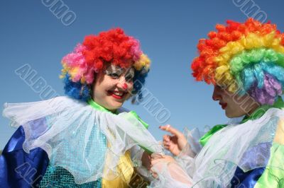 Two bizzare clowns in colored wigs upon blue sky