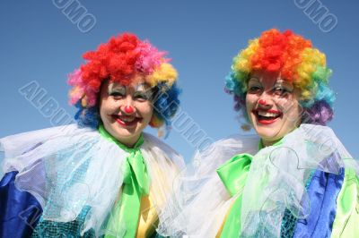Two bizzare clowns in colored wigs upon blue sky