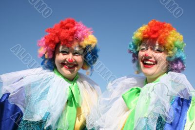 Two bizzare clowns in colored wigs upon blue sky