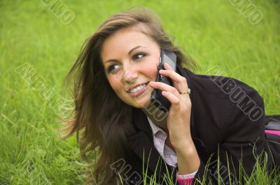 The girl speaks by phone laying on a green grass