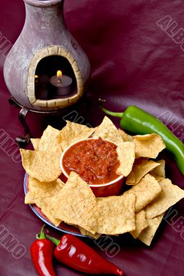 candle, chips, salsa and peppers on burgundy background