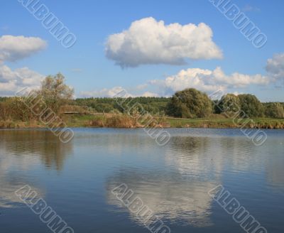 Cloudy sky over yellow autumn forest and pond