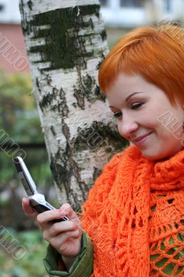 young red-haired woman in red scarf is sms in mobile-phone