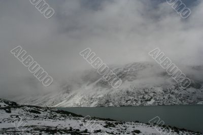 snow mountain in fog with cold lake