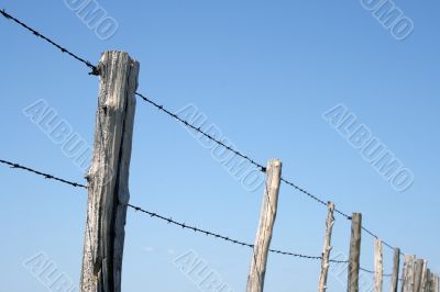 Barbed wire farm fence against blue sky