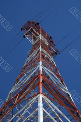 Red and white electricity pylon against the blue sky