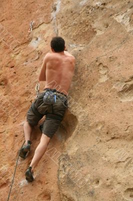 Bare back climber clinging to rock face