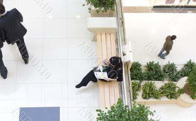 Girl sitting on bench and reading a magazine in a mall