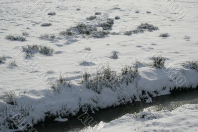 a field of snow and a small stream