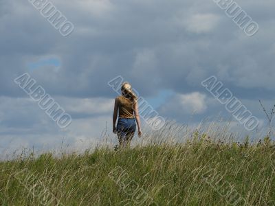 alone female figure in wide field uder cloudy sky