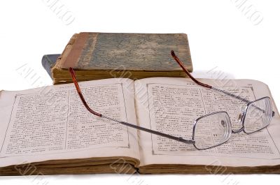 The open ancient book with glasses laying on it on a background