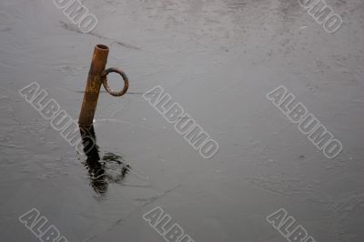 A rusty iron pole in the ice of a small lake