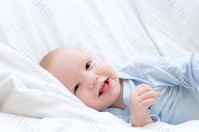 Little joyful baby resting on white bed