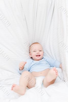 Little joyful baby fall on white bed