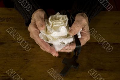 old hands with white rose and cross