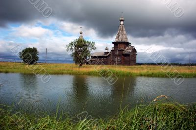 Ancient wooden church beyond the river with stormy sky
