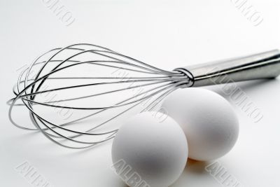 High contrast tilted view of a whisk and 2 eggs