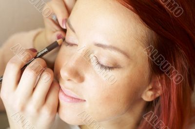 beautician is doing make-up to red-haired woman