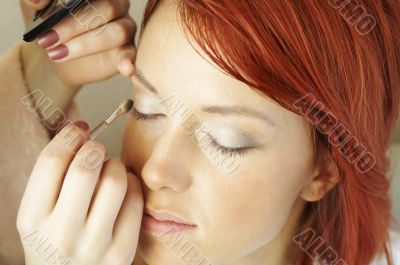 beautician is doing make-up to red-haired woman