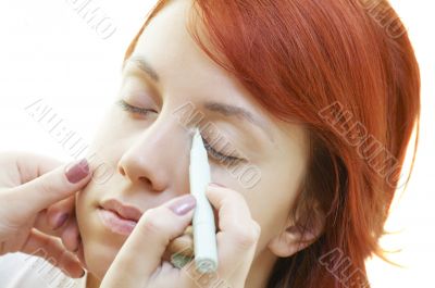 beautician is doing make-up to red-haired woman