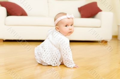 Eight month old baby girl seated on a hardwood floor