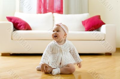 Happy eight month old baby girl seated on a hardwood floor